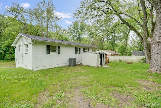 rear view of house with a shed, cooling unit, an outbuilding, brick siding, and view of wooded area