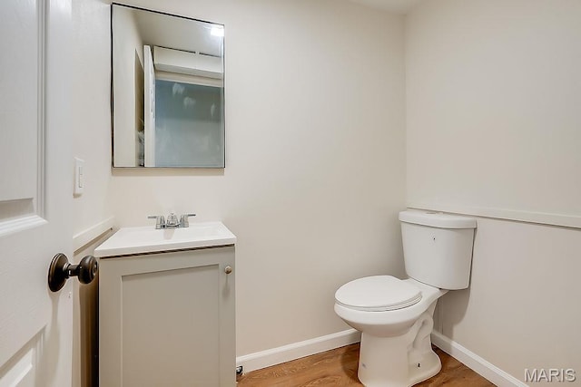 half bath featuring toilet, vanity, baseboards, and wood finished floors