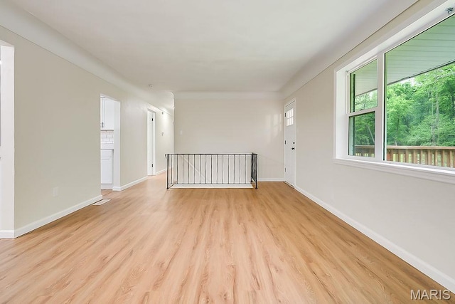 empty room featuring healthy amount of natural light, baseboards, and light wood-type flooring