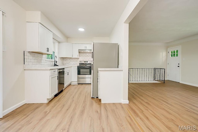 kitchen featuring stainless steel appliances, light countertops, light wood-type flooring, tasteful backsplash, and under cabinet range hood