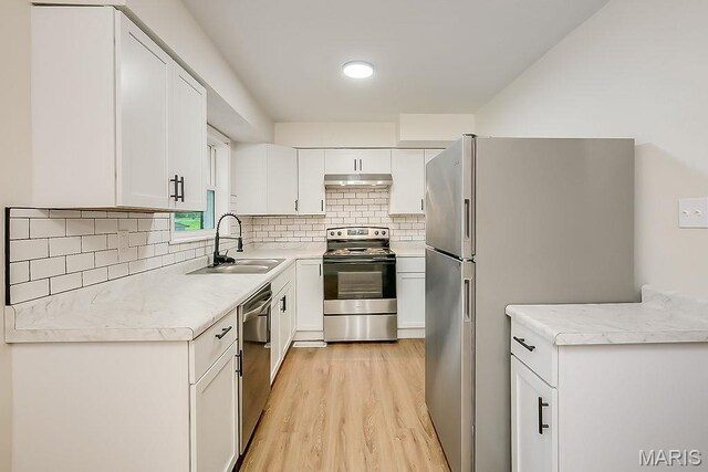 kitchen featuring stainless steel appliances, a sink, under cabinet range hood, light wood-style floors, and white cabinets