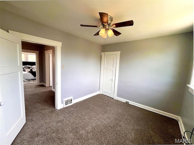 unfurnished room featuring dark colored carpet, a ceiling fan, and baseboards