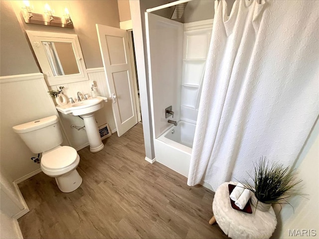 full bathroom with wood finished floors, toilet, shower / bath combo with shower curtain, and a wainscoted wall