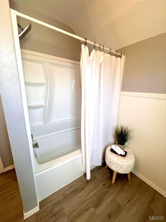 bathroom featuring wood finished floors, shower / bath combo, and baseboards