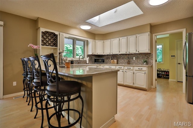 1989 Dogwood Trl, Collinsville, IL 62234 - kitchen featuring a skylight, appliances with stainless steel finishes, a peninsula, light wood-style flooring, and a breakfast bar