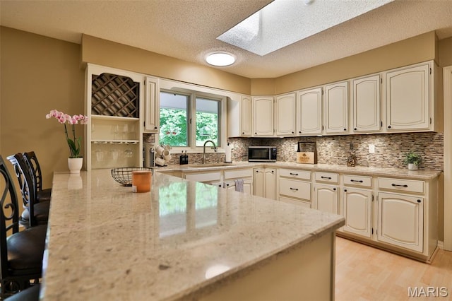 1989 Dogwood Trl, Collinsville, IL 62234 - kitchen with a skylight, a peninsula, a sink, tasteful backsplash, and light wood-style floors