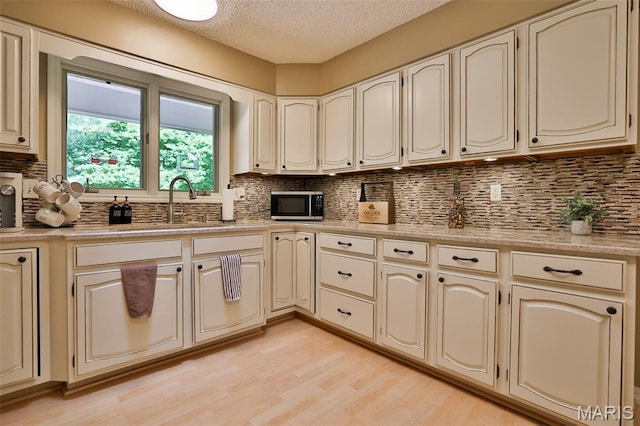 1989 Dogwood Trl, Collinsville, IL 62234 - kitchen with stainless steel microwave, cream cabinets, a textured ceiling, light wood-style floors, and backsplash