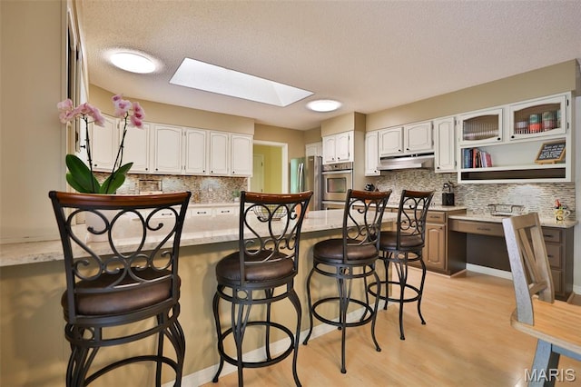 1989 Dogwood Trl, Collinsville, IL 62234 - kitchen featuring under cabinet range hood, a skylight, tasteful backsplash, a kitchen breakfast bar, and white cabinetry