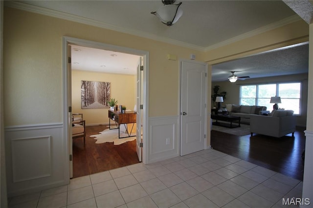 corridor with light wood-style flooring, ornamental molding, and wainscoting