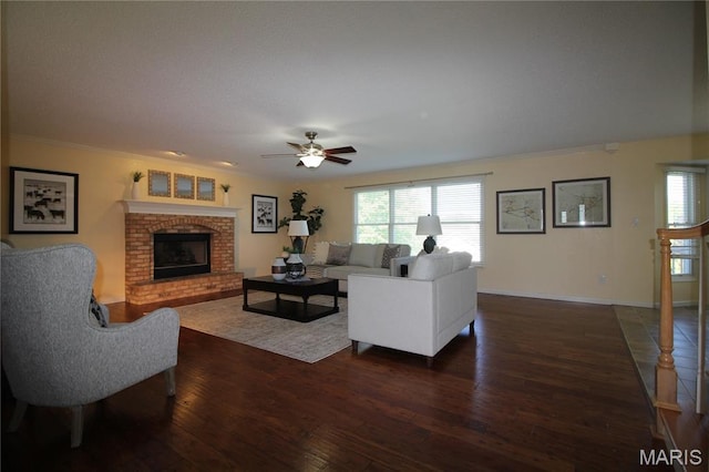 living area featuring dark wood-style flooring, a brick fireplace, ceiling fan, plenty of natural light, and ornamental molding