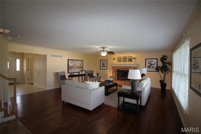 living room featuring a textured ceiling, ceiling fan, a brick fireplace, ornamental molding, and wood finished floors