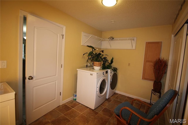 laundry room with washing machine and clothes dryer, a textured ceiling, baseboards, and dark tile patterned flooring