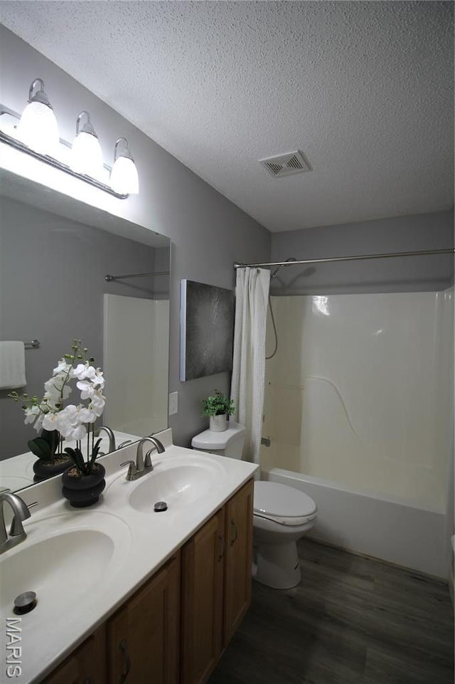 full bath with wood finished floors, a textured ceiling, shower / bath combo, toilet, and double vanity
