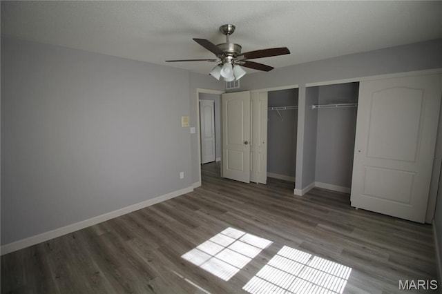 unfurnished bedroom with two closets, baseboards, wood finished floors, and a ceiling fan