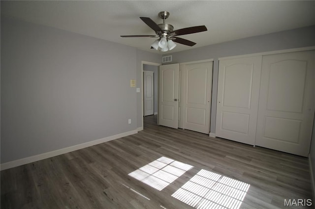 unfurnished bedroom with baseboards, multiple closets, wood finished floors, and a ceiling fan