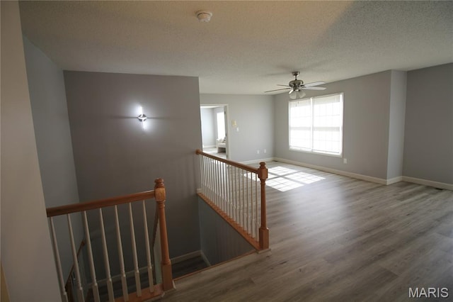 stairs featuring wood finished floors, baseboards, a textured ceiling, and ceiling fan