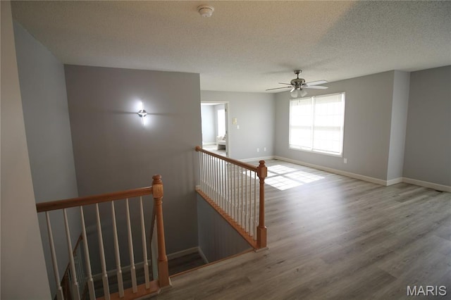 stairs featuring wood finished floors, a textured ceiling, baseboards, and ceiling fan
