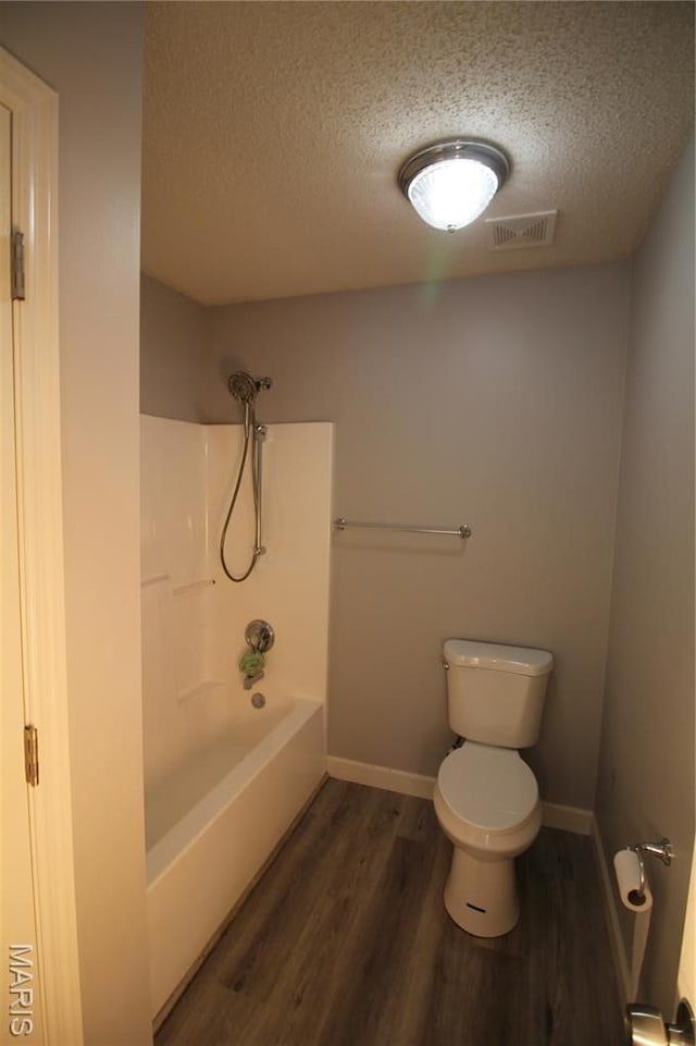 bathroom featuring a textured ceiling, wood finished floors, toilet, shower / tub combination, and baseboards