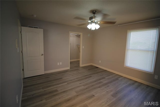 unfurnished bedroom with baseboards, wood finished floors, a walk in closet, and a ceiling fan
