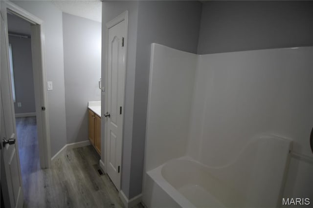 full bathroom featuring wood finished floors, a bath, vanity, baseboards, and a shower
