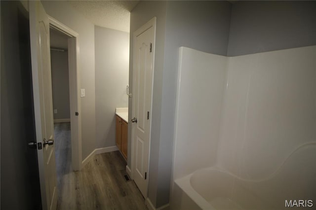 bathroom featuring wood finished floors, vanity, a bath, baseboards, and a shower