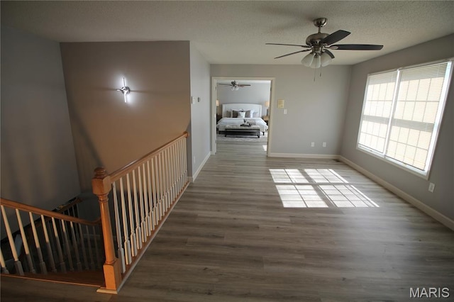 hallway featuring baseboards, wood finished floors, and a textured ceiling