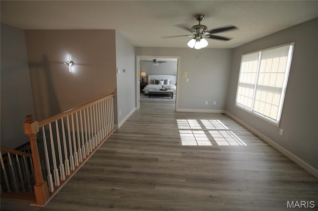 unfurnished living room featuring a ceiling fan, wood finished floors, baseboards, and a textured ceiling