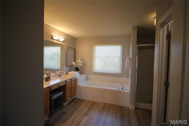 bathroom with wood finished floors, a textured ceiling, a stall shower, a garden tub, and vanity