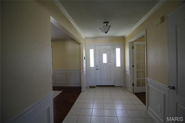 foyer entrance with a textured ceiling, a textured wall, ornamental molding, wainscoting, and a decorative wall