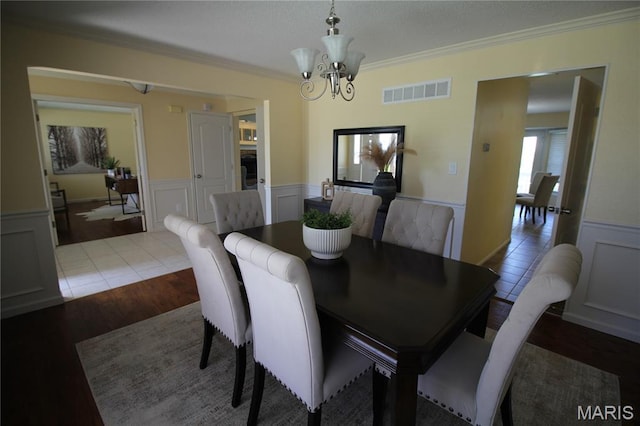 dining room featuring a wainscoted wall, a chandelier, ornamental molding, a decorative wall, and wood finished floors