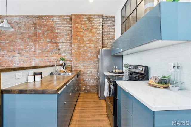 2713 Utah St, Saint Louis, MO 63118 - kitchen with stainless steel range with electric stovetop, a sink, brick wall, light wood-style flooring, and blue cabinetry