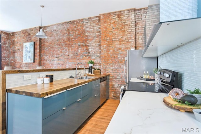 2713 Utah St, Saint Louis, MO 63118 - kitchen featuring a sink, appliances with stainless steel finishes, light wood-type flooring, brick wall, and a wood stove