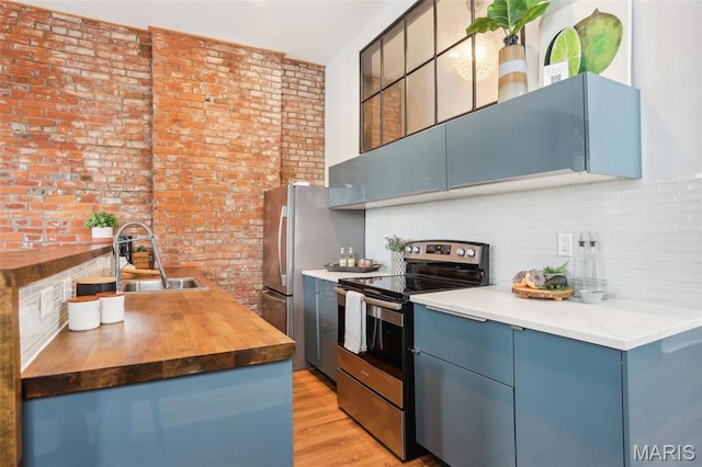2713 Utah St, Saint Louis, MO 63118 - kitchen featuring stainless steel appliances, wood counters, a sink, blue cabinets, and brick wall