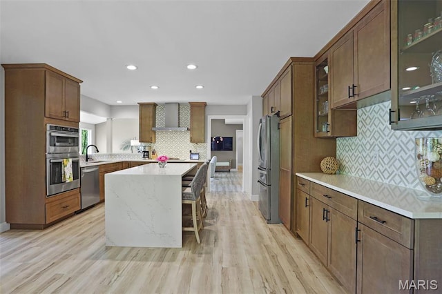 kitchen featuring appliances with stainless steel finishes, wall chimney range hood, tasteful backsplash, light wood-style flooring, and recessed lighting