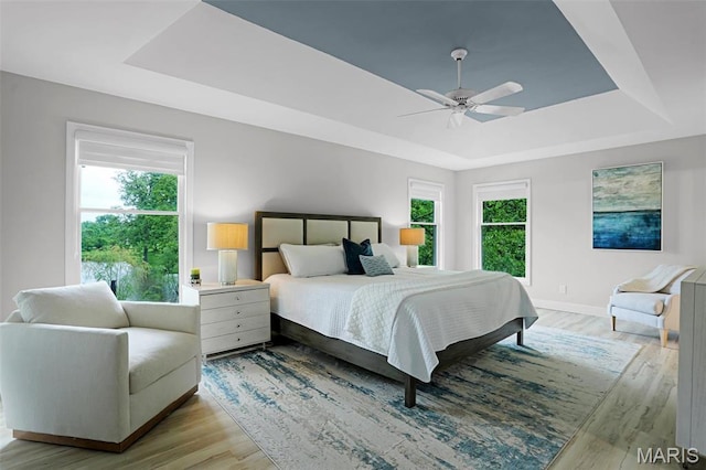 bedroom featuring a raised ceiling, light wood finished floors, baseboards, and ceiling fan