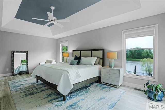 bedroom featuring a tray ceiling, light wood finished floors, baseboards, and a ceiling fan