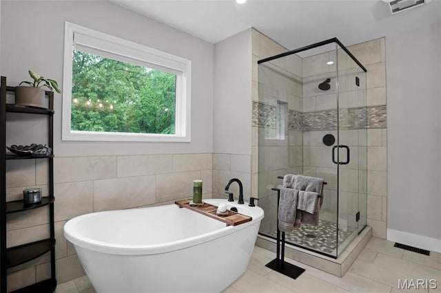 bathroom with a soaking tub, a stall shower, tile walls, and tile patterned flooring