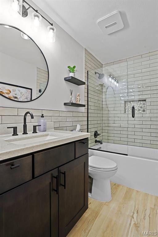 full bathroom featuring wood finished floors, toilet, vanity, combined bath / shower with glass door, and tile walls