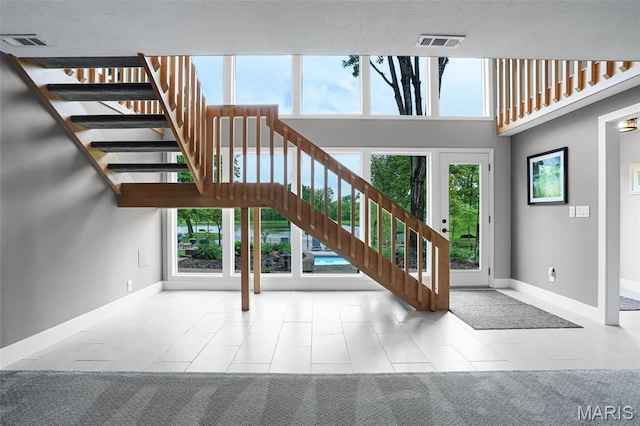 stairs featuring baseboards, healthy amount of natural light, tile patterned flooring, and a high ceiling