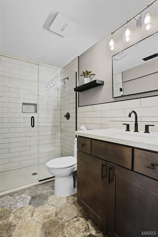 bathroom featuring tile walls, stone finish flooring, toilet, a stall shower, and vanity