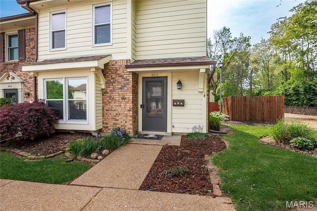 view of exterior entry with fence and brick siding