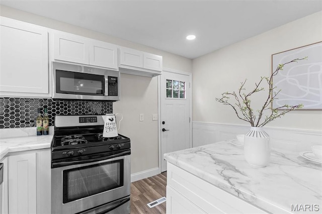 7211 Kensington Ave, Maplewood, MO 63143 - kitchen with appliances with stainless steel finishes, white cabinets, light stone counters, wood finished floors, and backsplash