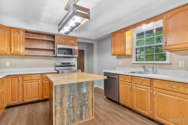 kitchen featuring appliances with stainless steel finishes, a sink, light wood-type flooring, and decorative backsplash