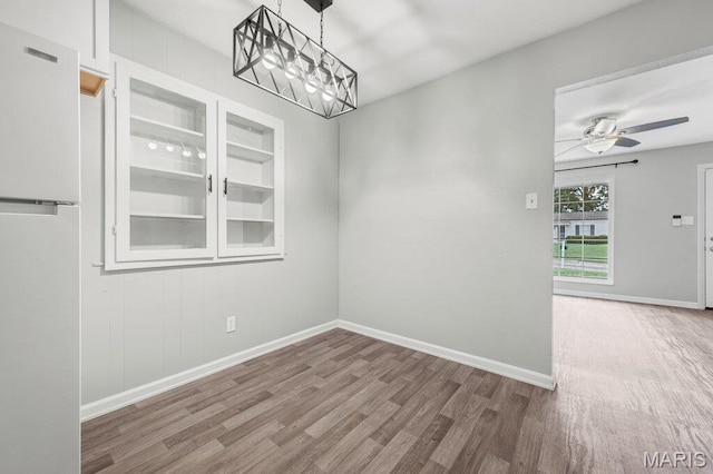 unfurnished dining area with wood finished floors, baseboards, ceiling fan, a chandelier, and built in shelves
