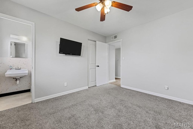 unfurnished bedroom featuring carpet flooring, a sink, baseboards, ensuite bathroom, and a ceiling fan
