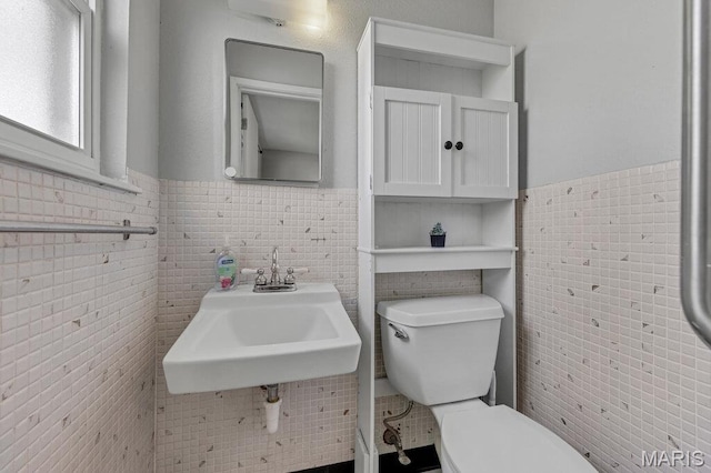 bathroom with toilet, wainscoting, tile walls, and a sink