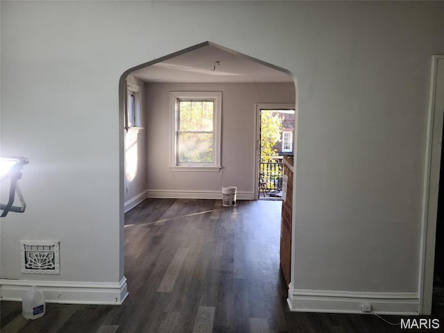 corridor with arched walkways, dark wood finished floors, and baseboards