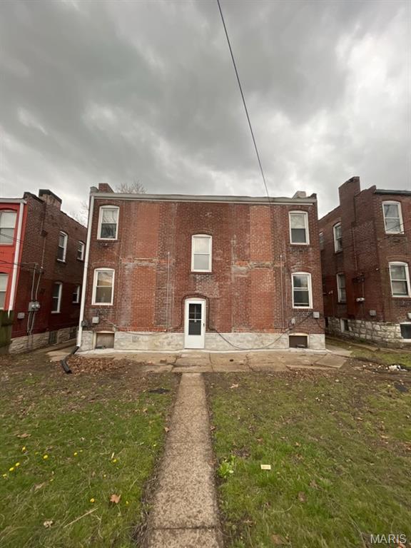 rear view of property featuring a lawn and brick siding