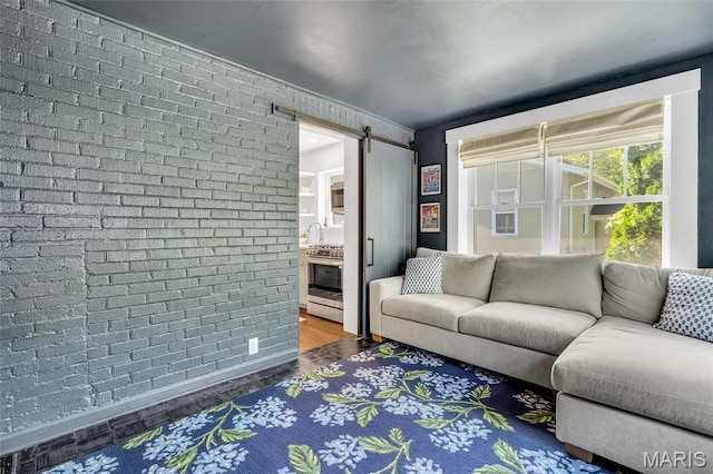 living room featuring a barn door, brick wall, and dark wood-type flooring