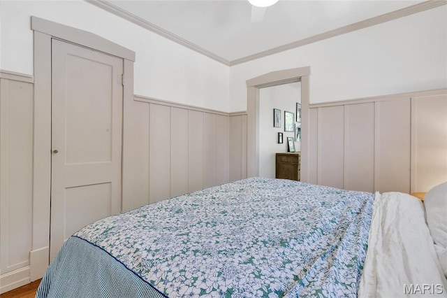 bedroom with a wainscoted wall, a decorative wall, ornamental molding, a ceiling fan, and wood finished floors